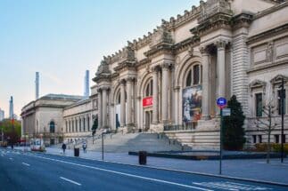 Metropolitan Museum of Art building seen from the street, with the beautiful architecture, bustling streets, & pedestrians