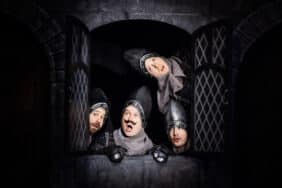 Three men posing at a castle window in the musical theater show titled 'Spamalot'