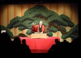 A storyteller in a red kimono captivates the audience with tales in the performance of 'Katsura Sunshine’s Rakugo'