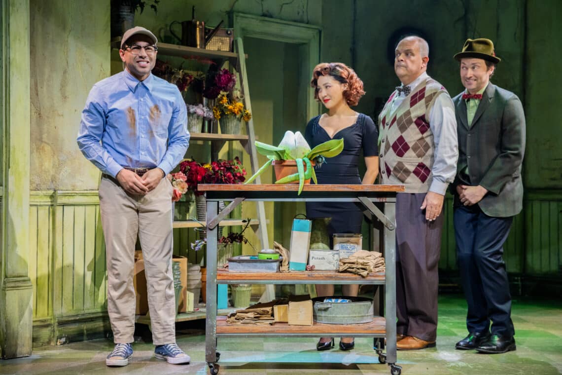 Three men and a woman conversing in a plant shop in the musical theater Little Shop of Horrors