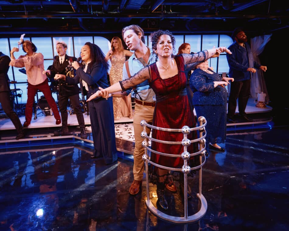 Stage scene from Titanique with actors in mid-performance, including a couple mimicking the Titanic bow pose