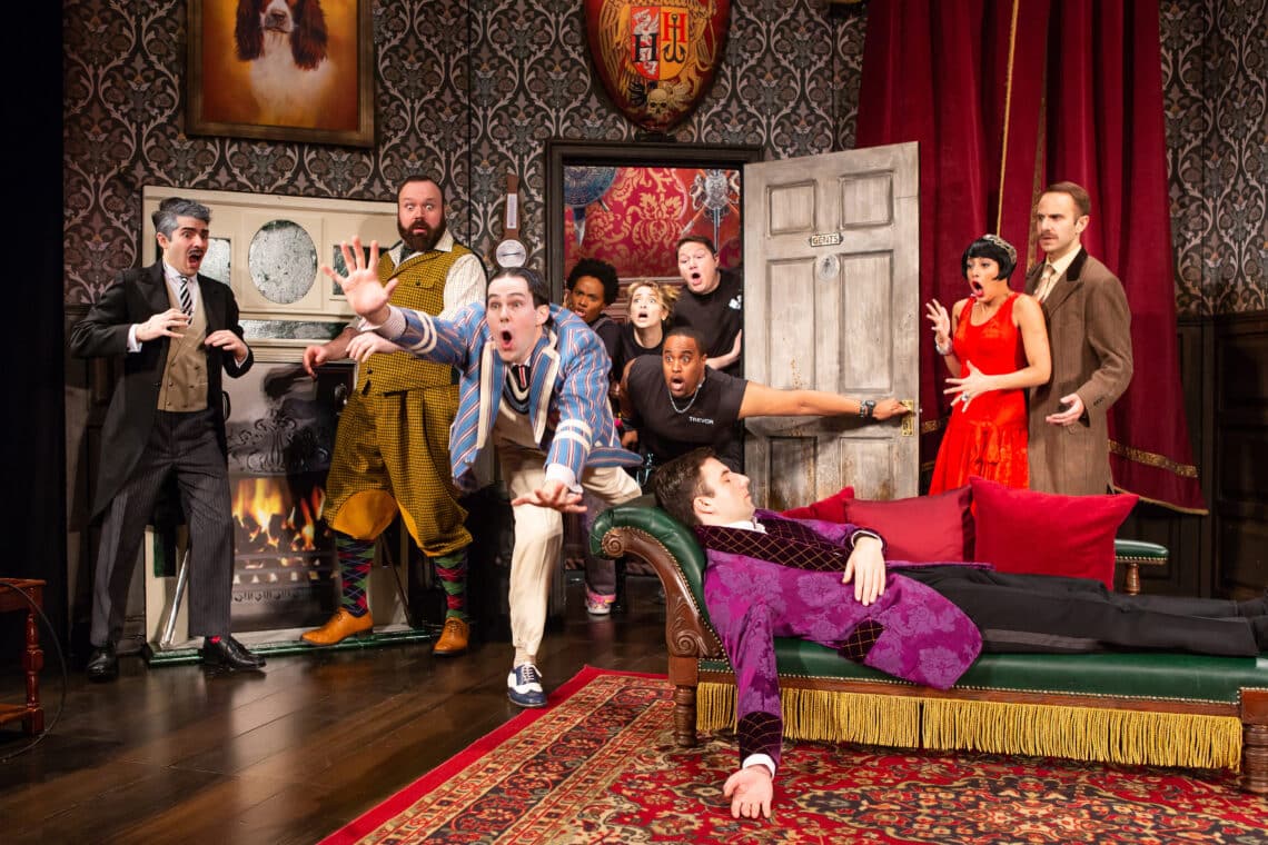 Scene from The Play That Goes Wrong featuring actors in a chaotic and comedic moment, with one lying on a couch