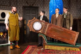 Scene from The Play That Goes Wrong with actors reacting to a large grandfather clock that has fallen onto a couch