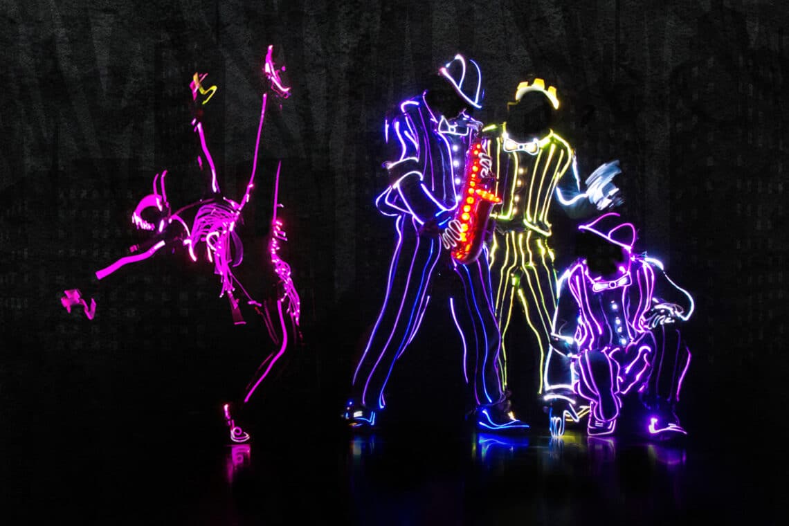 Neon-outlined dancers perform on a dark stage, creating vibrant light patterns in the iLuminate show