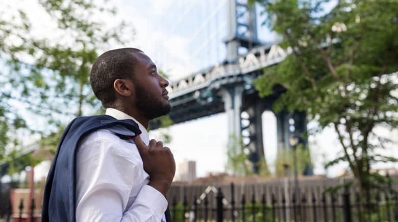A man walking in Brooklyn Dumbo Park with Manhattan Bridge in the background