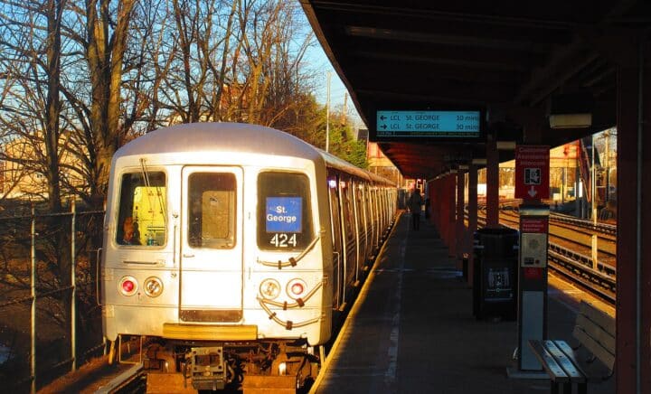Train on Staten Island Railway pulling into a station at sunset, with a platform and bare trees nearby