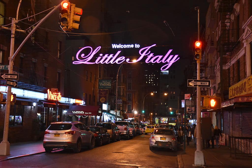 Little Italy's vibrant street scene at night, featuring the illuminated welcome sign and bustling activity