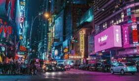 Times Square in NYC with colorful lights from billboards and signs, amidst a continuous flow of cars and pedestrians