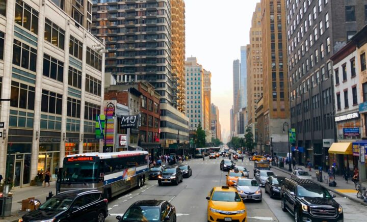 Traffic scene in New York City featuring various vehicles and high-rise buildings along the road