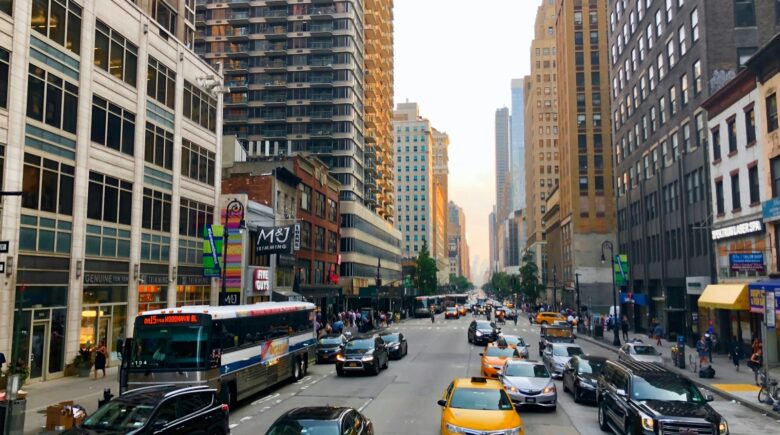 Traffic scene in New York City featuring various vehicles and high-rise buildings along the road