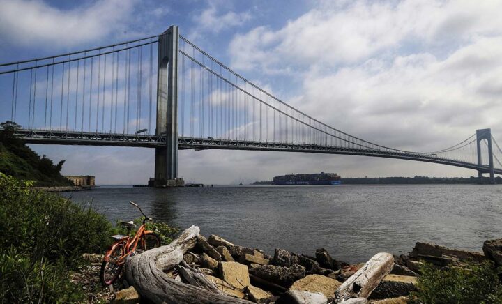 Container vessel passing the Verrazano Bridge in New York city, with an orange bicycle in foreground view from richmond county staten island