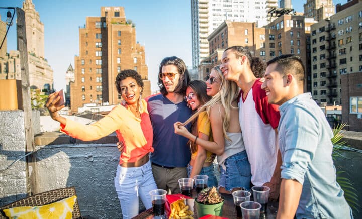 A group of friends enjoying drinks at a rooftop bar with NYC buildings in the background, capturing one of the best Top 10 NYC Activities to experience and a must-do for your NYC Bucket List when exploring Things to Do in New York City.