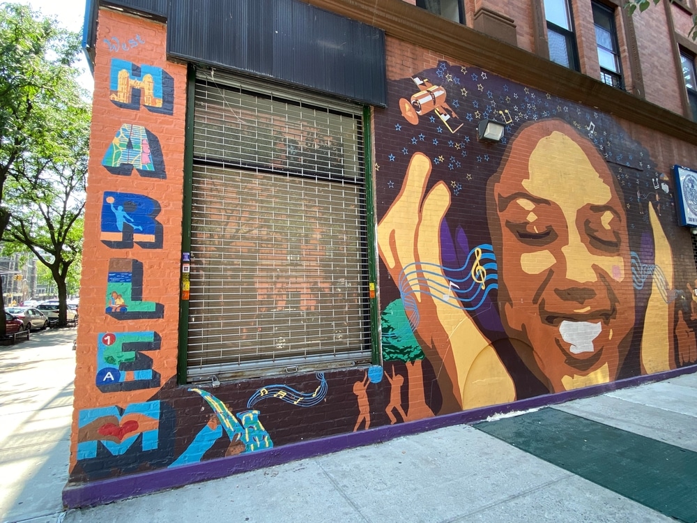 New York, NY USA - August 20, 2023 : Colorful mural with word "Harlem" and face of a smiling young woman listing to music on headphones on corner of a brick building in Harlem, New York City, USA