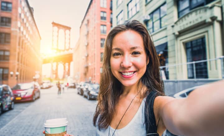 A smiling woman taking a selfie in New York, Brooklyn Bridge in the background