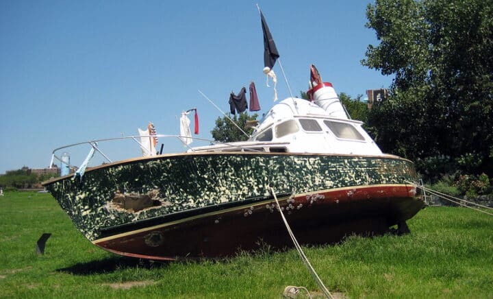 A weathered boat displayed on grass at Socrates Sculpture Park