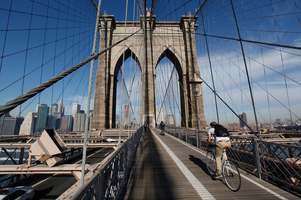 Bicyclist heading to Manhattan on the Brooklyn Bridge in morning light with blue sky and wispy clouds