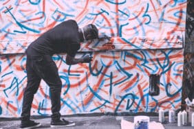 Street artist creating graffiti art on a wall in Bushwick, Brooklyn, using red, blue, and orange spray paint