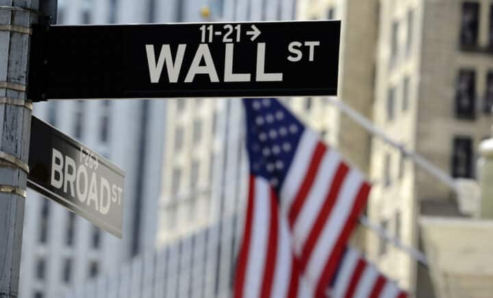 Wall Street sign and American flag, set against the backdrop of skyscrapers in New York City