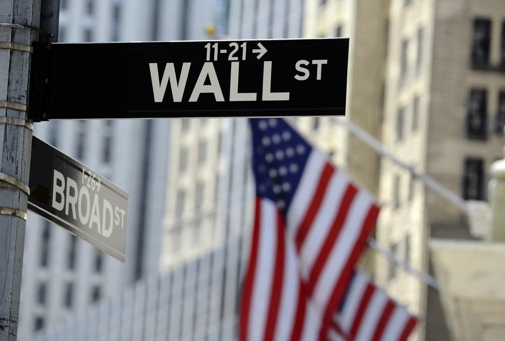 Wall Street sign and American flag, set against the backdrop of skyscrapers in New York City