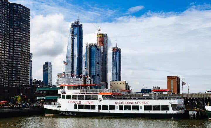 Sightseeing ferry docked in New York City with tall buildings under construction in the background on a clear day