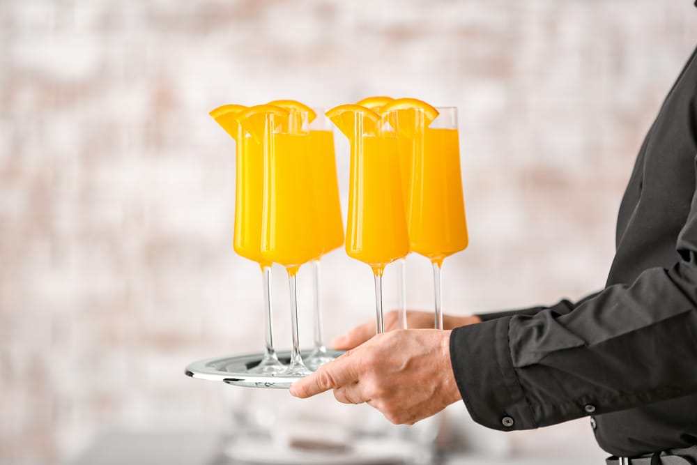 Waiter with glasses of tasty mimosa cocktail