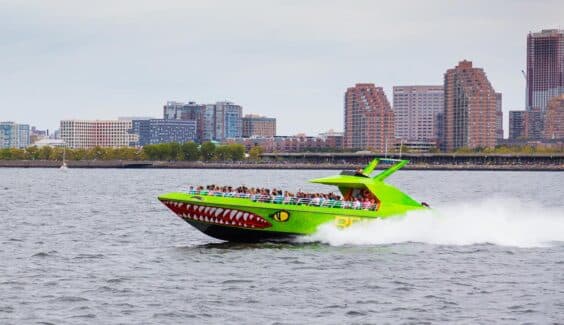 A green speedboat crosses the Hudson River with New York City buildings in the background