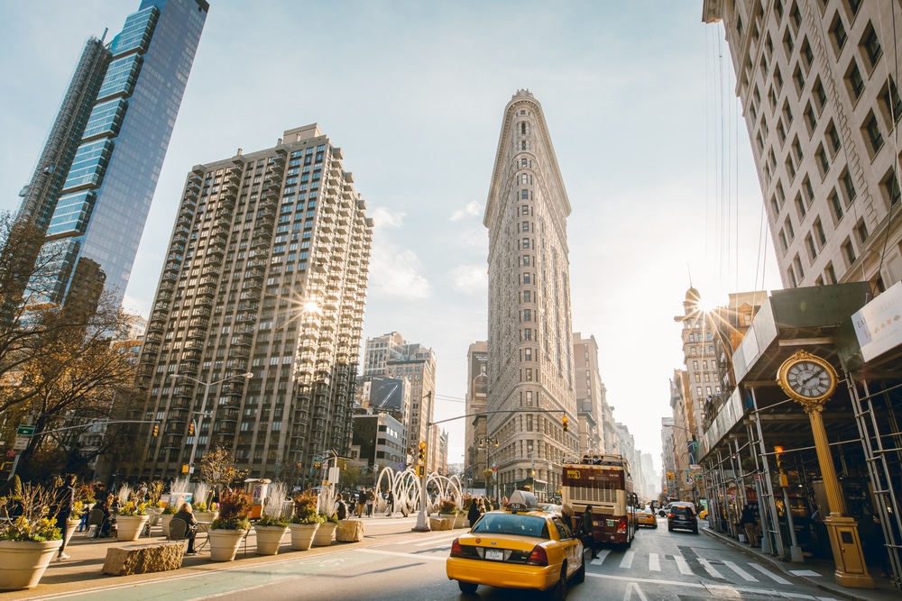 Flat Iron building facade, one of the first skyscrapers ever built, with NYC Fifth Avenue and taxi cabs