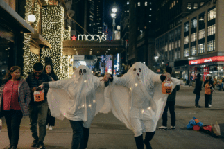 People dressed as ghosts in NYC holding jack-o-lantern buckets while others walk on the pavement