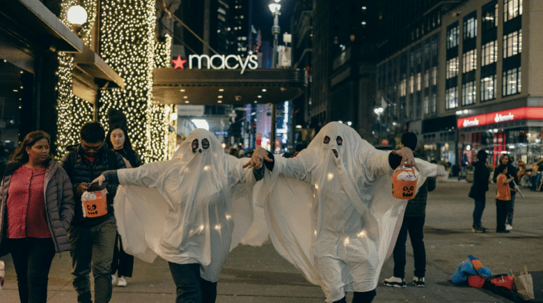 People dressed as ghosts in NYC holding jack-o-lantern buckets while others walk on the pavement