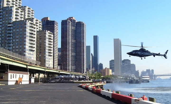 A helicopter tour of NYC comes to an end as a black helicopter hovers over the water during its descent, with the city skyline visible in the background