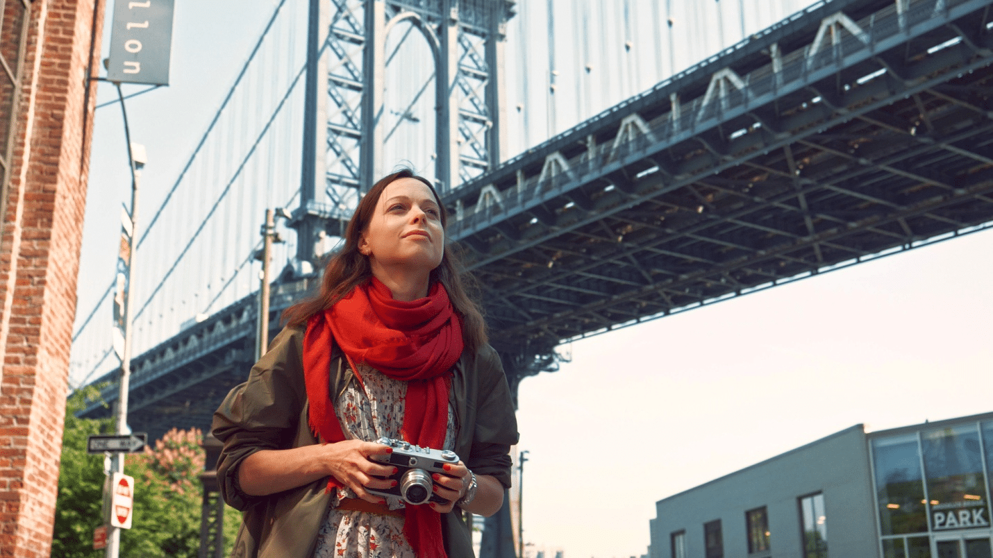 A woman holding a camera walking along the Brooklyn Bridge