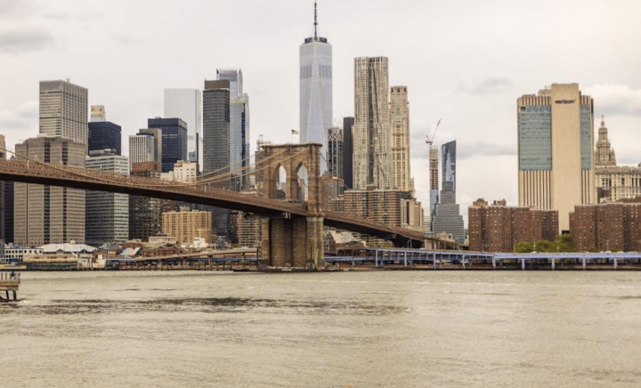 A scenic view of the Brooklyn Bridge in New York City, spanning the East River with the Manhattan skyline in the background