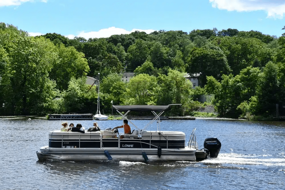 A boat is seen on the Hudson River during a unique NYC day tour with trees and buildings beyond it.