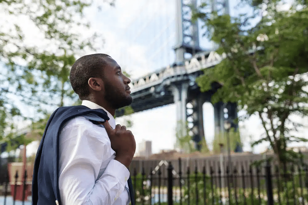 A man in a white shirt holds his jacket while looking out into the distance in DUMBO during a unique NYC day tour