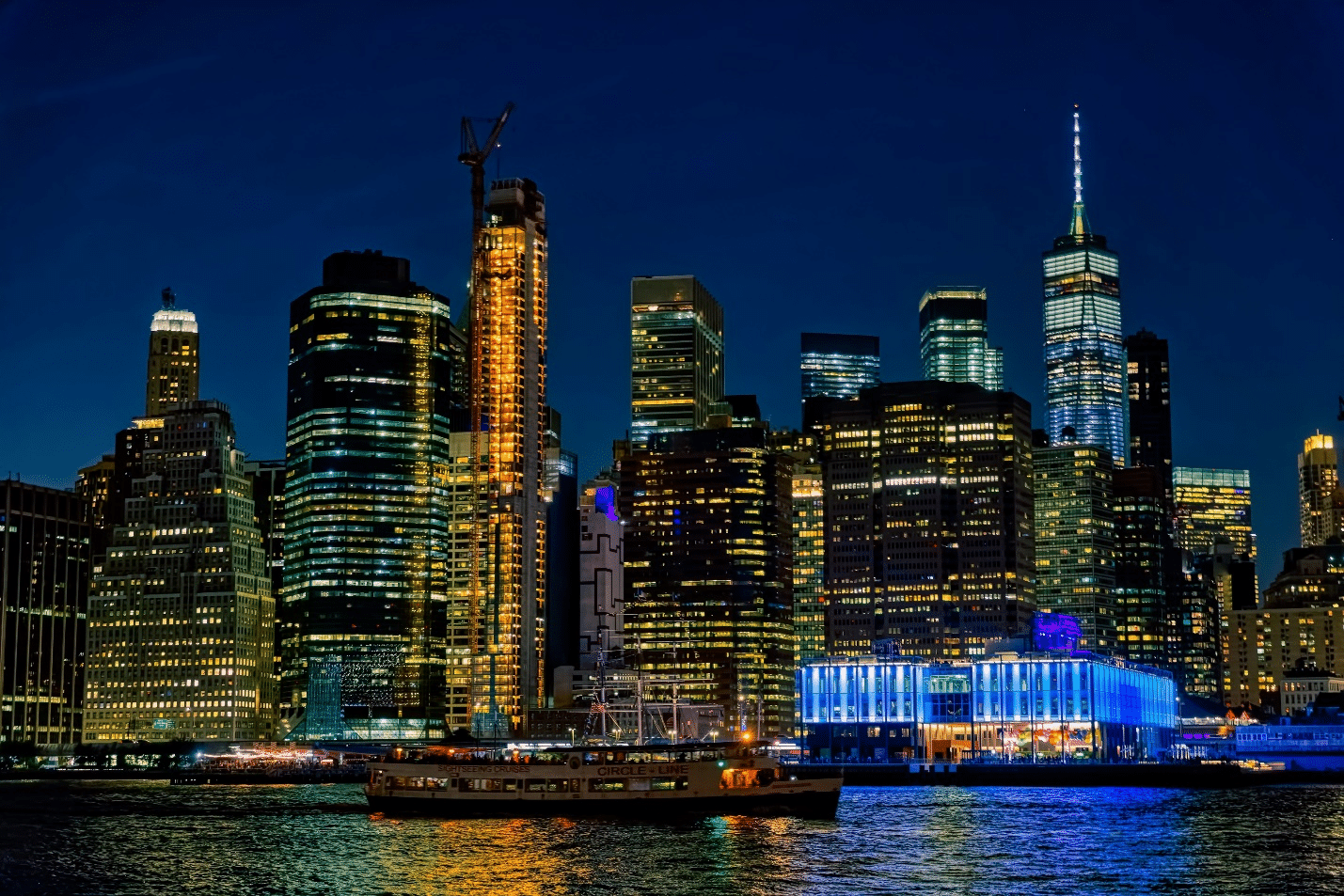 The NYC skyline at night seen with the water in front and the Circle Line passing by showing the view from a NYC dinner cruise