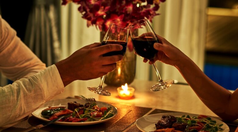 A close-up of a couple holding wine glasses while having dinner at a restaurant