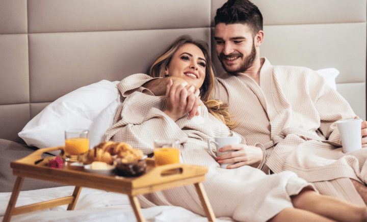 A young, happy couple enjoying breakfast in a luxury hotel room.