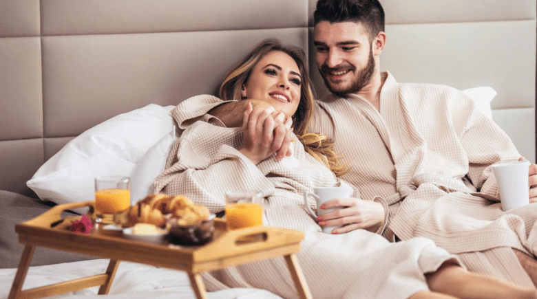 A young, happy couple enjoying breakfast in a luxury hotel room.