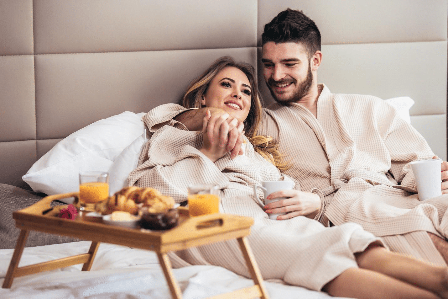 A young, happy couple enjoying breakfast in a luxury hotel room.