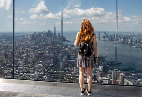 A girl gazing out from the glass windows of The Edge at the Manhattan skyline.