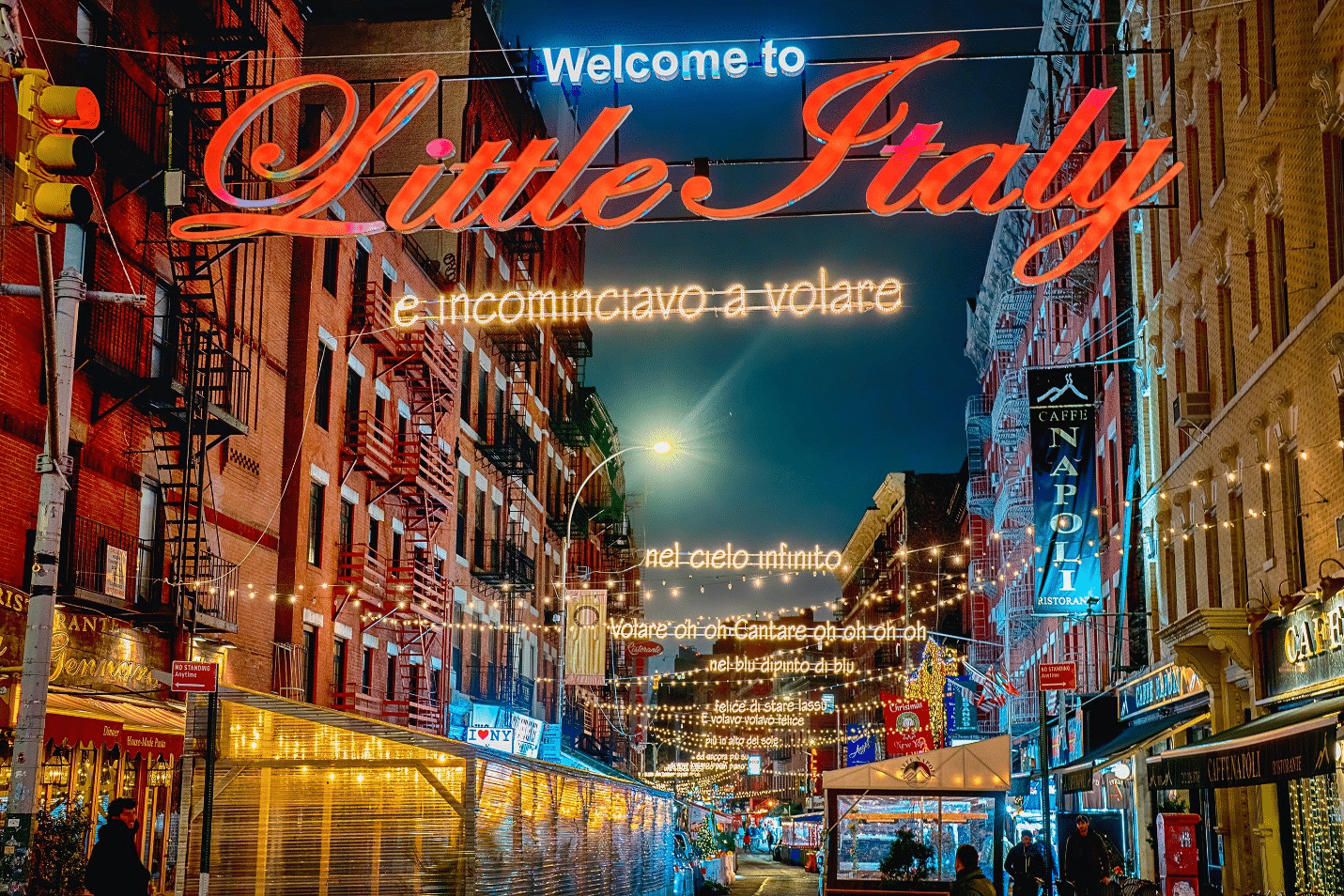 A lively street in Little Italy, NYC, with restaurants, lights, and Italian flags.