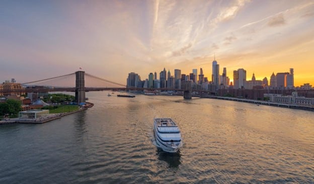 A yacht sailing past the Manhattan skyline during sunset