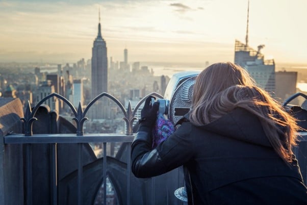 A woman looking through binoculars at the New York City skyline.