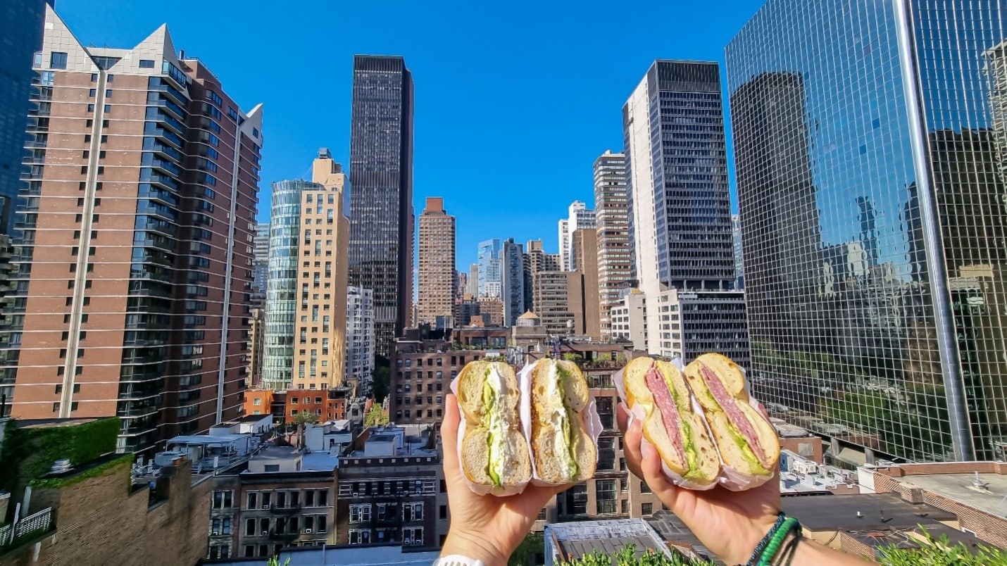 Two people holding bagel sandwiches during aone-day sightseeing tour