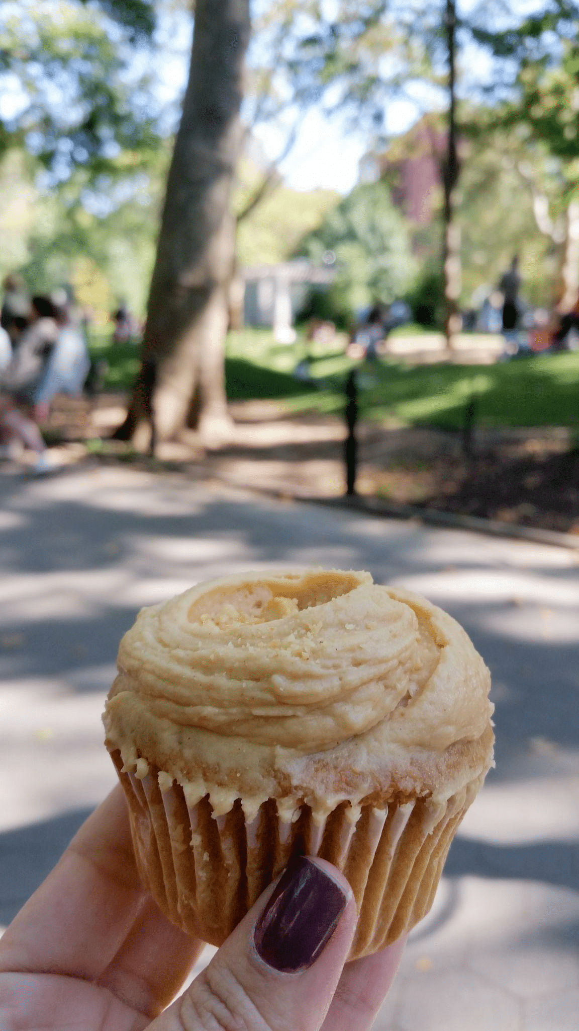A person enjoys a cupcake in a park.