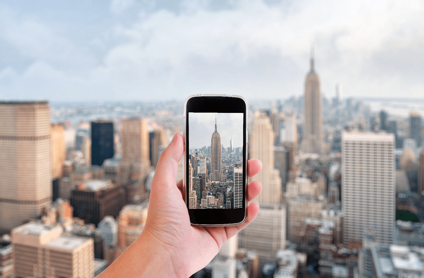 A person holding a picture on their phone of the Empire State Building during acity trip to New York