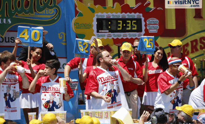 People eating hotdogs with their scores being held up behind their heads
