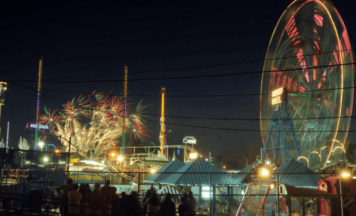 A Ferris wheel with fireworks in the back