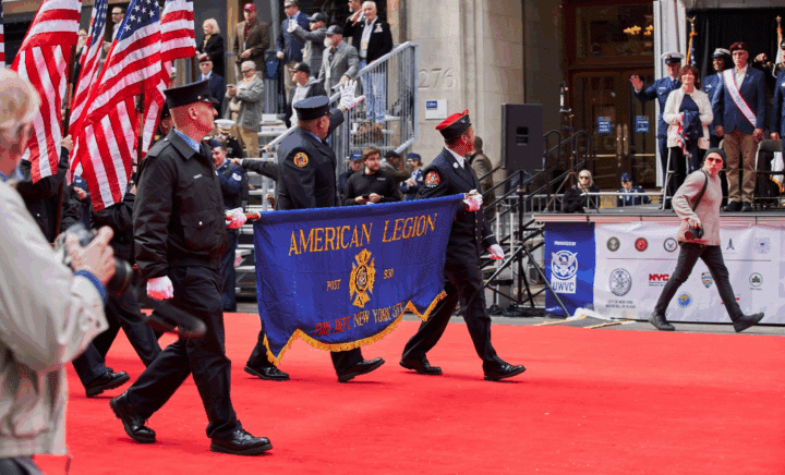 Men in uniform carrying a banner for the American Legion Independence Day Parade