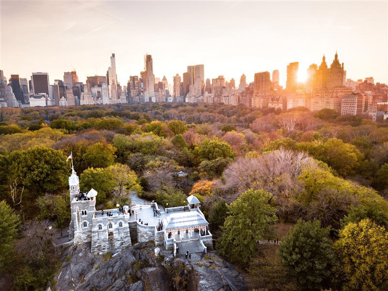 Belvedere Castle and park at sunset, with city buildings behind.